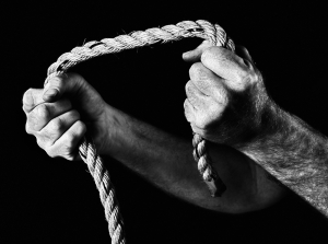 Masculine hands grip rope, pulling apart. Black and white.